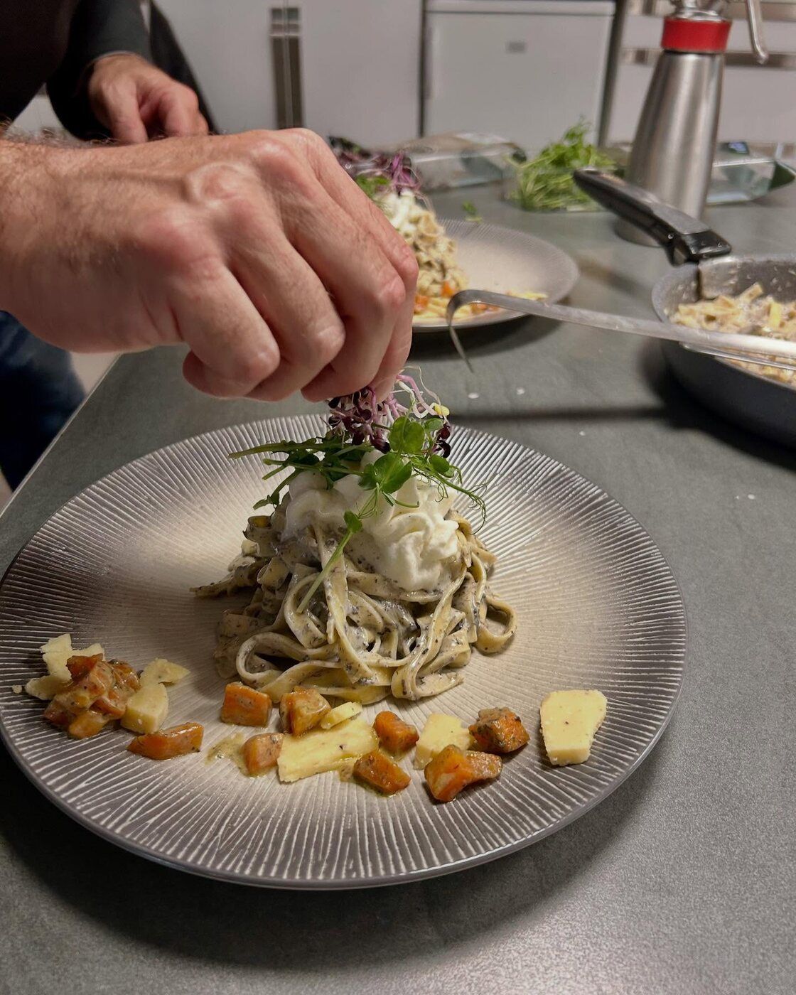 Une main dépose des jeunes pousses sur un nid de tagliatelles à la crème de truffe couronné de burrata